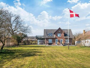 Ein großes Backsteinhaus mit einem geneigten Dach, einer Fahnenstange mit einer Flagge und einem Rasen.