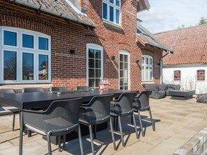 A patio with a long table and chairs, a sofa, and a small table with a bottle and glass. - 8 Person Holiday Home in Bjert (Bjert)
