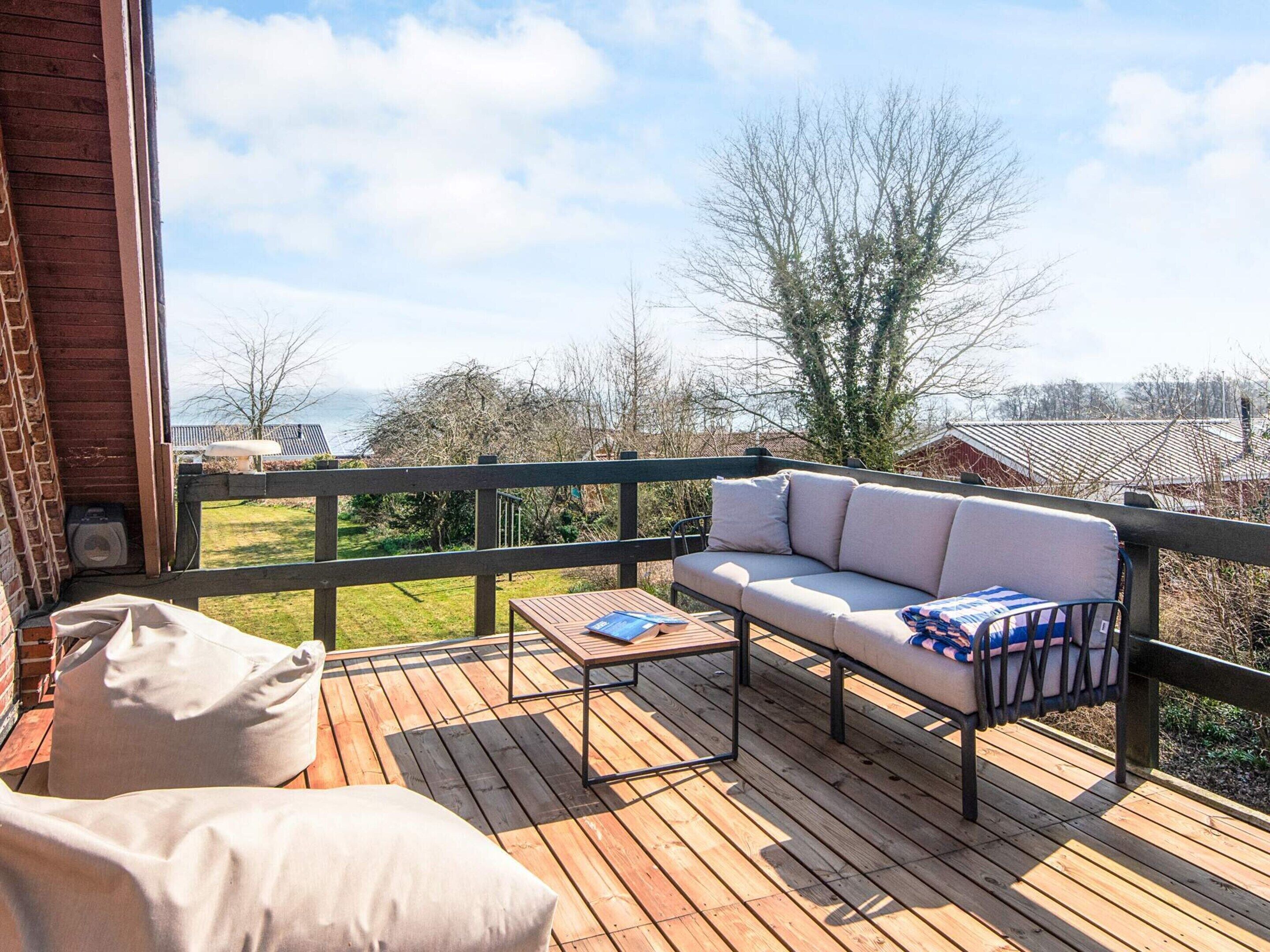 A wooden deck with a sofa and cushions, a small table, and a view of the landscape.
