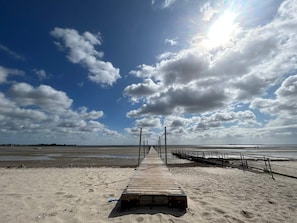 A wooden pier leading to a beach with a clear sky and clouds.
