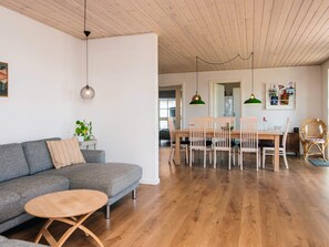 A modern living room with a grey sofa, a round wooden coffee table, and a dining area with a wooden table and chairs.