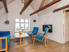A room with a wooden ceiling, a round table, two blue chairs, a sofa, a TV, and a window with a view. - 8 Person Holiday Home in Bjert (Bjert)