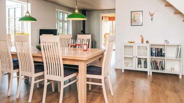A dining area with a wooden table and chairs, a staircase, and a bookshelf with books and decorative items. - 8 Person Holiday Home in Bjert (Bjert)
