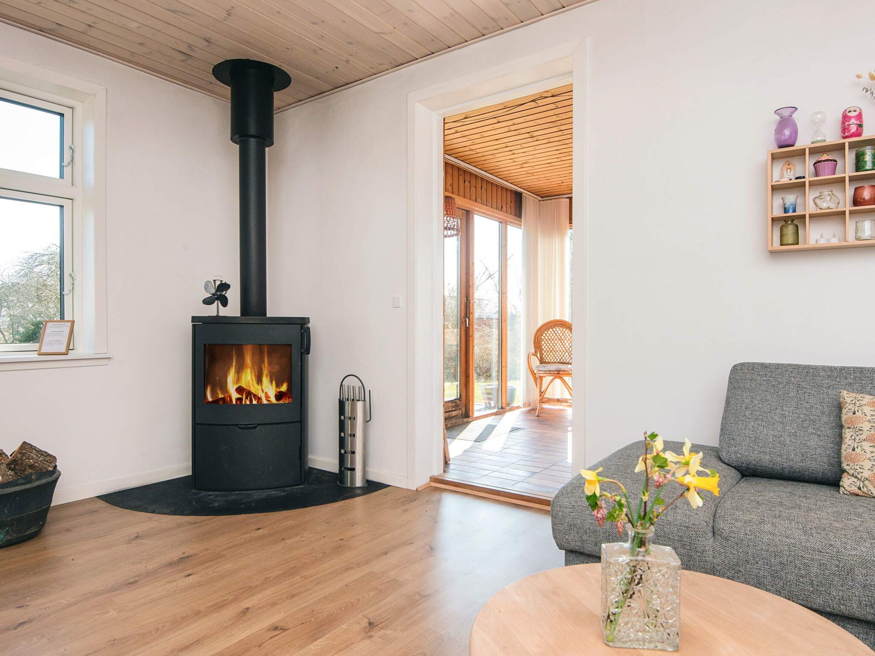 A modern living room with a wood-burning stove, a grey sofa, and a wooden coffee table.