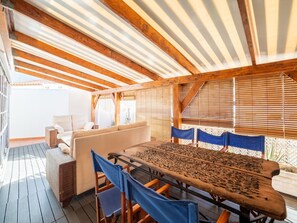 A covered outdoor seating area with a wooden table and chairs, a sofa, and a view through wooden blinds. - Belvilla by OYO Apartment in Adeje (Adeje)