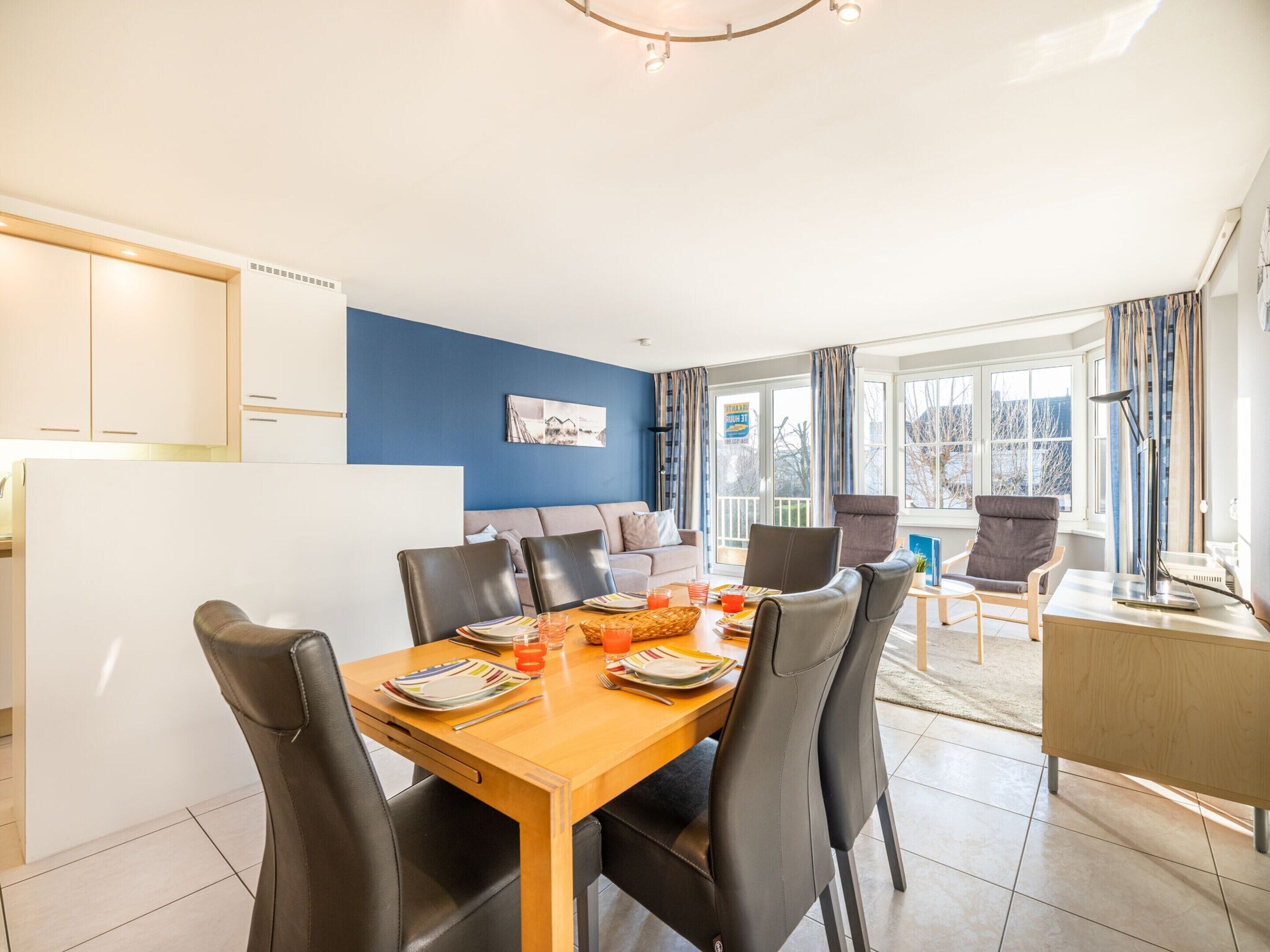 A modern dining area with a wooden table set for four, surrounded by black chairs.