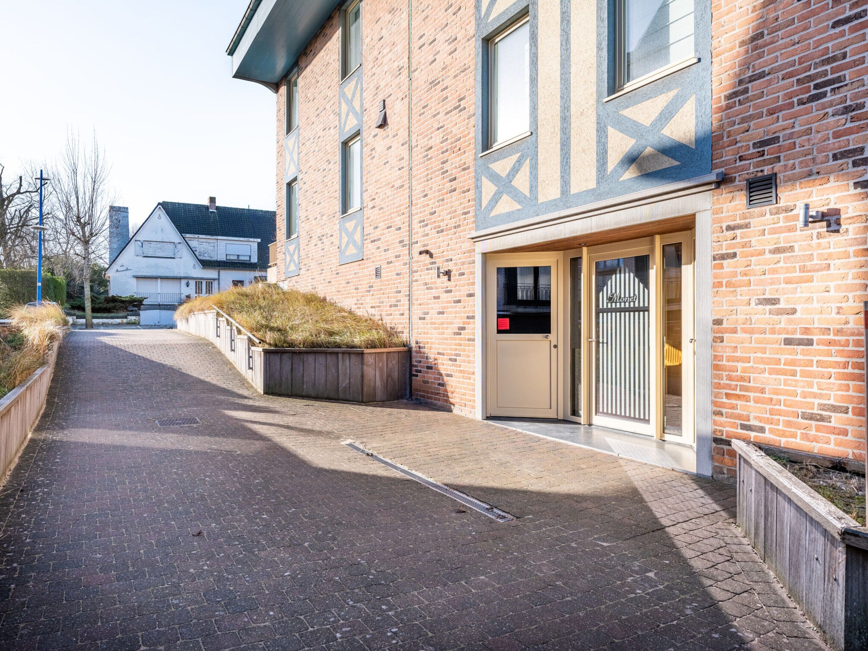A brick building with a gated entrance, a small garden area, and a paved pathway leading to the entrance.