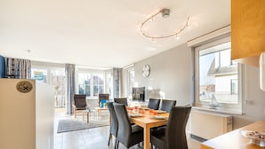 Un espace de restauration moderne avec une table en bois, des chaises noires et une grande fenêtre donnant sur des immeubles.