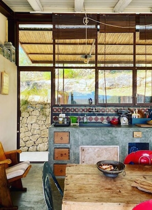 Una cocina rústica con pared de piedra, una mesa de madera y ventana con vista a un jardín.