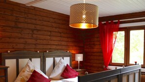 Ein Zimmer in einer Holzhütte mit einem Bett, einer Hängelampe und einem Fenster mit roten Vorhängen.