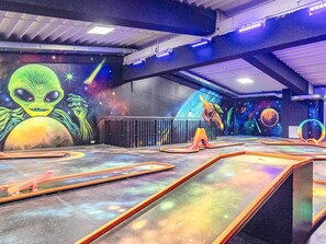 Een binnenruimte met een muurschildering uit de ruimte, met daaronder een alien en planeten, en een speelruimte met een raket en kleurrijke speeltoestellen.