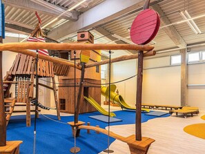Een kinderspeelplaats met een houten klimstructuur, glijbanen en zachte speekvormen.
