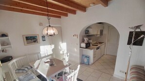 Une cuisine chaleureuse avec un coin repas, dotée d’un plafond en bois, de murs blancs et d’un sol carrelé.