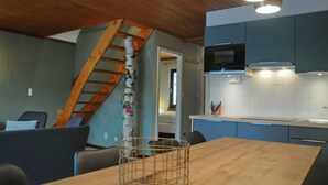Een moderne keuken met een houten plafond, een inbouwmagnetron en een houten eettafel met een mand van draad.