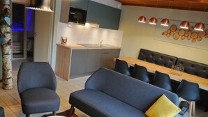 Een moderne woonkamer met een bank, stoelen, een eettafel en een keuken op de achtergrond.