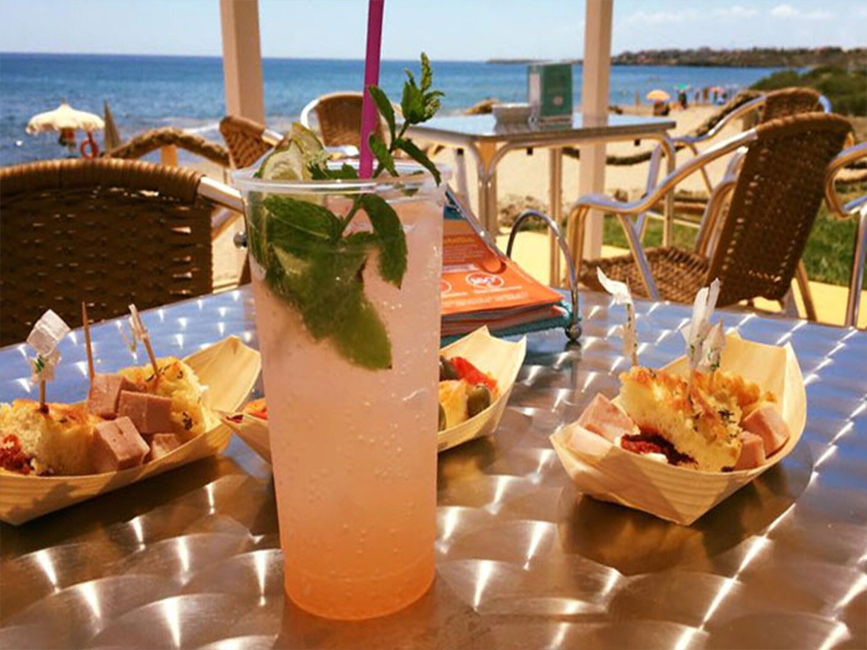 A table with a drink, food baskets, and a view of the beach.
