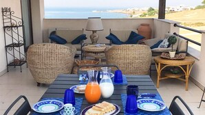 A dining area with wicker furniture, a table set with plates, glasses, and a pitcher of orange juice. - Apartment With Garden in Resort With Pool (Isola di Capo Rizzuto)