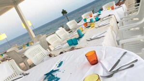 A beachside dining area with white plastic chairs and tables, starfish decorations, and a view of the ocean. - Apartment With Garden in Resort With Pool (Isola di Capo Rizzuto)