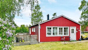 Une maison en bois rouge avec une porte et des fenêtres blanches, une cheminée et une petite terrasse.