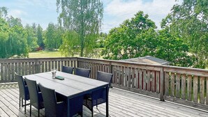 Une terrasse en bois avec une table et des chaises, entourée d’une balustrade en bois.