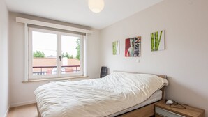A bedroom with a bed, bedside table, and a window with a view of buildings outside. - La Boheme 204 G1 Stylish Apartment in Koksijde (Koksijde)