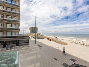 Une promenade bordée d’un bâtiment à toit de verre, une structure moderne au design original, et une plage en arrière-plan.