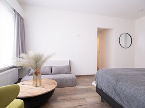 Une chambre d’hôtel moderne avec un lit, une table ronde en bois, un canapé et un miroir au mur.