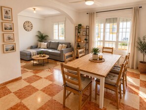 A living room with a sofa, a dining table with chairs, a clock on the wall, and a window with curtains. - Casa Chajay - Sun & Relax Cabo Roig (Orihuela)
