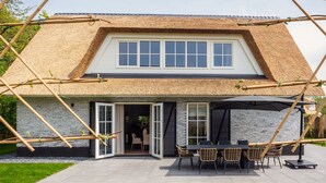 A modern house with a thatched roof, a patio with outdoor furniture, and a brick exterior. - Villa on Texel Near Beach and Forest (De Koog)