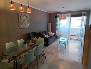 A modern living room with a glass dining table, teal chairs, a dark sofa, and a large abstract painting. - Belvilla by OYO Apartment in Fuengirola (Fuengirola)