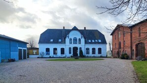En stor, hvid bygning med en symmetrisk facade, en midterindgang og en grusvej, der fører op til den.