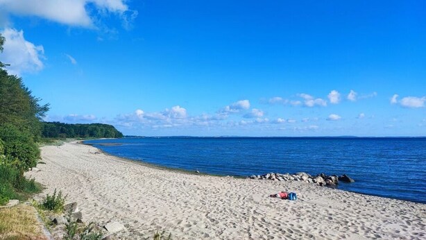 En strand med klar himmel, sandet bred og en person, der ligger på sandet.