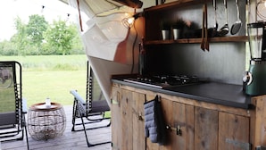 Una cocina rústica al aire libre con encimera de madera, utensilios colgantes y vistas a un campo cubierto de césped.