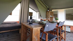 Un comedor con toldo, una mesa dispuesta para cuatro personas, un farol y un aparador de madera con vajilla.