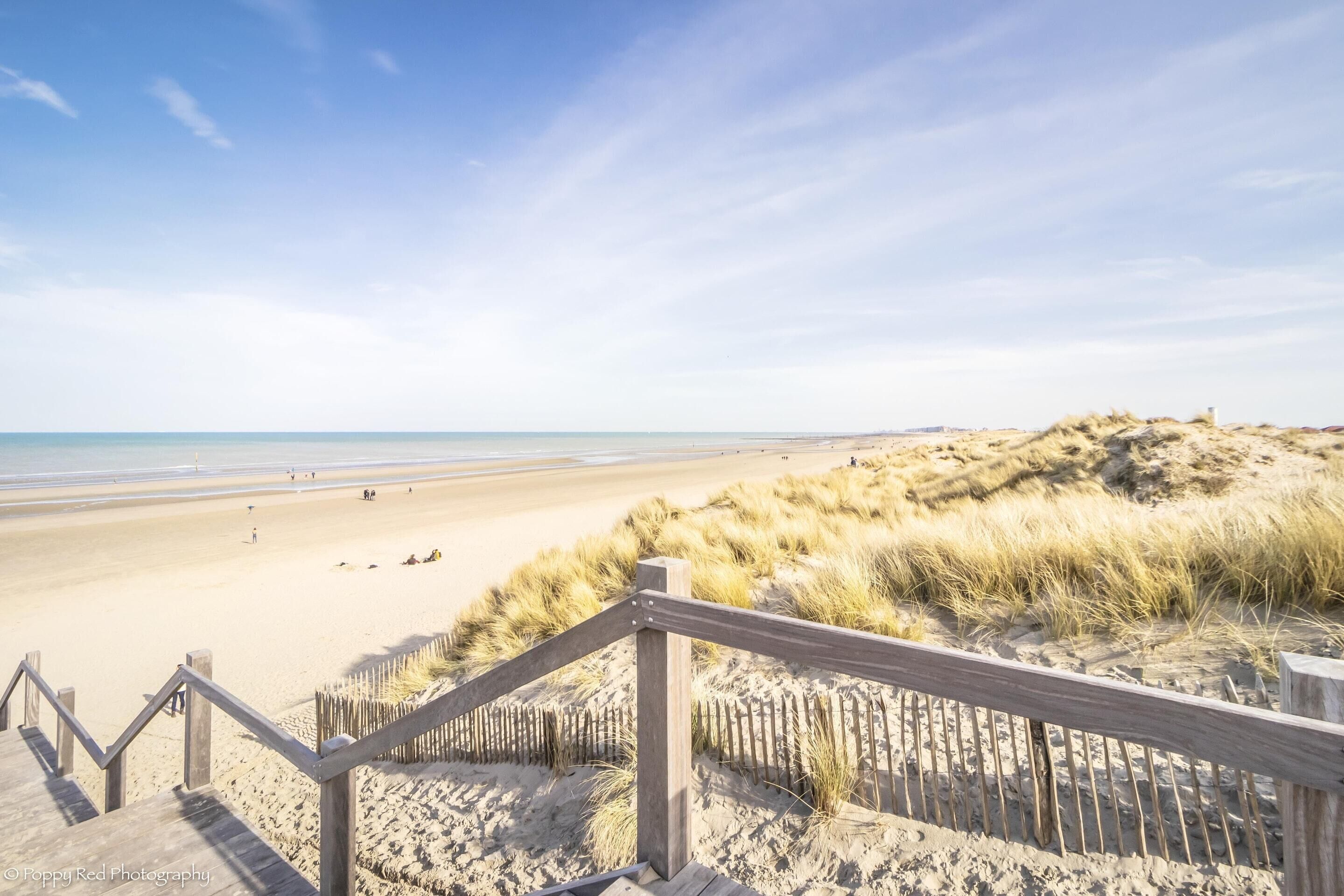 Een strand met een houten trap die naar het zand leidt, een zandduin en de oceaan op de achtergrond.