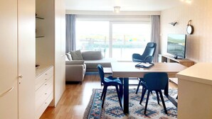 Un salon moderne comprenant un canapé, une table à manger avec des chaises, un téléviseur et une grande fenêtre avec des rideaux.