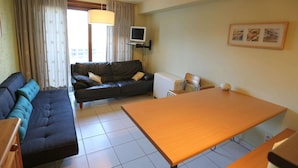 A living room with a sofa, a dining table, and a TV. - Stylish Stay by the Seafront (Middelkerke)