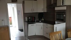 Een kleine keuken met witte kastjes, een zwart aanrecht en een houten eettafel.