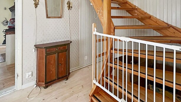 Une pièce avec un escalier en bois, une rambarde blanche, un meuble en bois et un miroir accroché au mur.