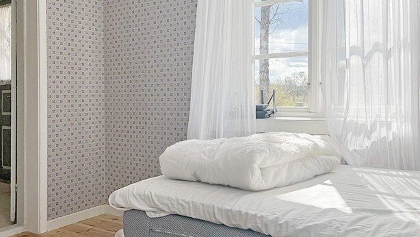 A bedroom with a bed, a window with sheer curtains, and a patterned wall. - 4 Person Holiday Home in Moheda (Moheda)