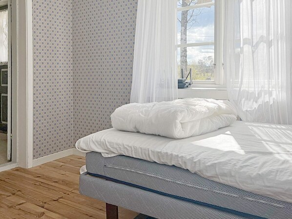 A bedroom with a bed, a window with sheer curtains, and a patterned wall.