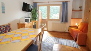 A cozy room with a bed, a desk, a television, and a window with curtains. - Apartment in Tropolach With Sauna (Hermagor-Pressegger See)