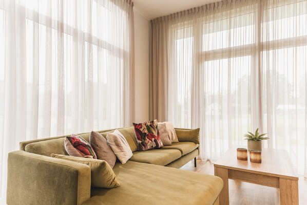 A living room with a sofa, pillows, a coffee table, and sheer curtains. - Chalet in Zuna by Tennis Court (Zuna)