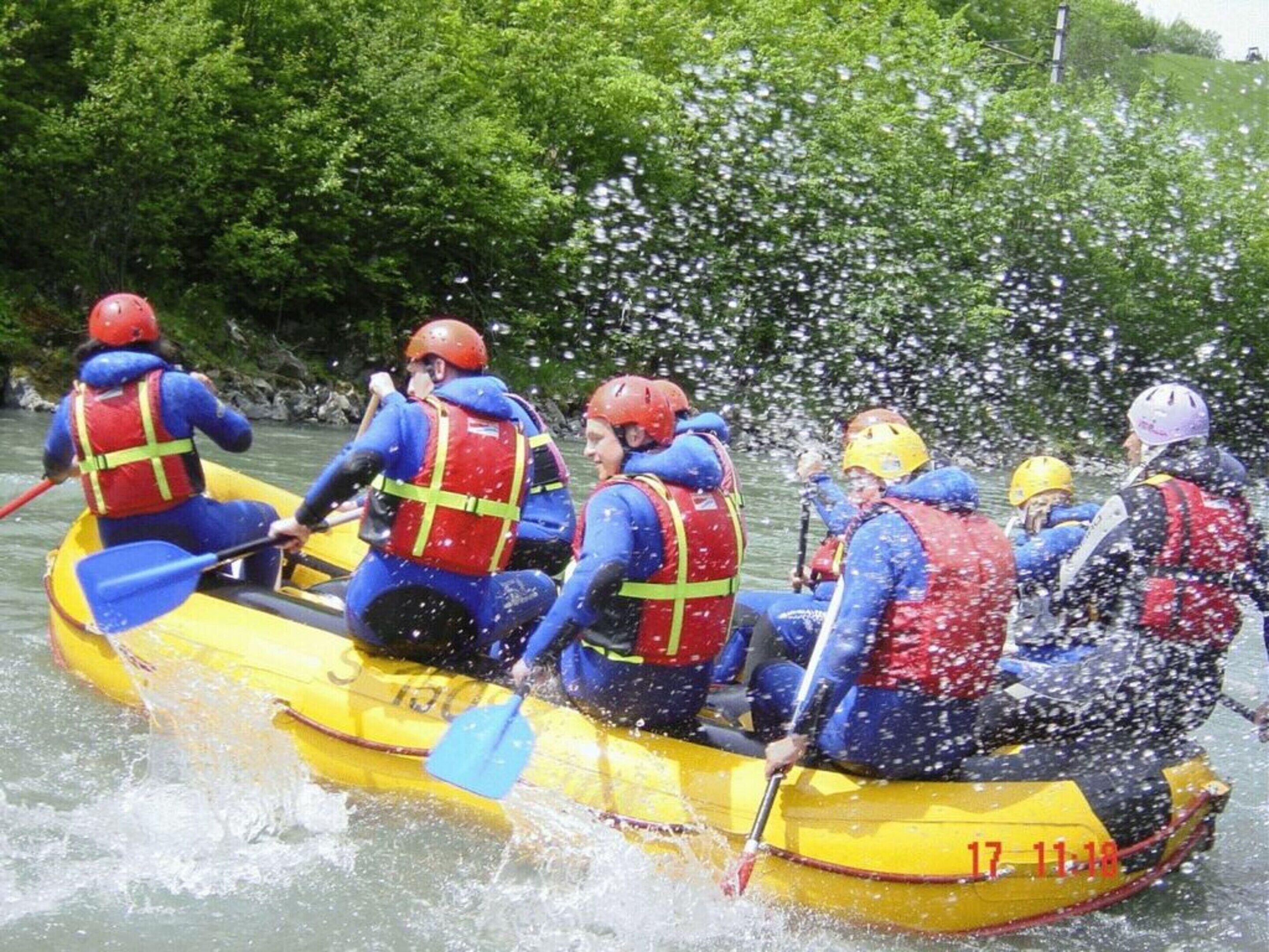Eine Gruppe von Menschen in einem gelben Schlauchboot mit roten Rettungswesten paddelt durch das Wasser.