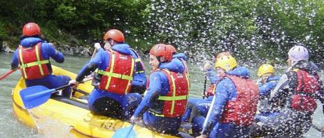 A group of people in a yellow raft with red life jackets, paddling through water.