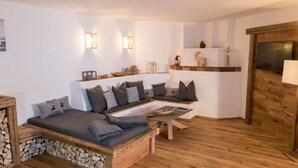 A cozy living room with a wooden floor, a sofa with cushions, a coffee table, and a fireplace with a TV. - Chalet Yuma 4 People (Mauterndorf)