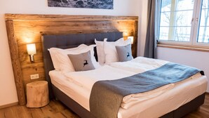 A neatly made bed with a wooden headboard, a bedside lamp, and a window with curtains. - Chalet Yuma 4 People (Mauterndorf)
