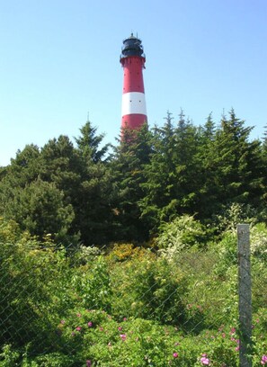 A lighthouse surrounded by dense green trees and a chain-link fence. - Rum Hart II - Apartment 5 (Hörnum (Sylt))
