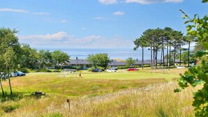 A grassy field with a goalpost, trees, and a view of the sea.