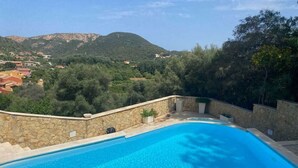 Piscina com muro de pedra e vista para uma aldeia e montanhas ao fundo.